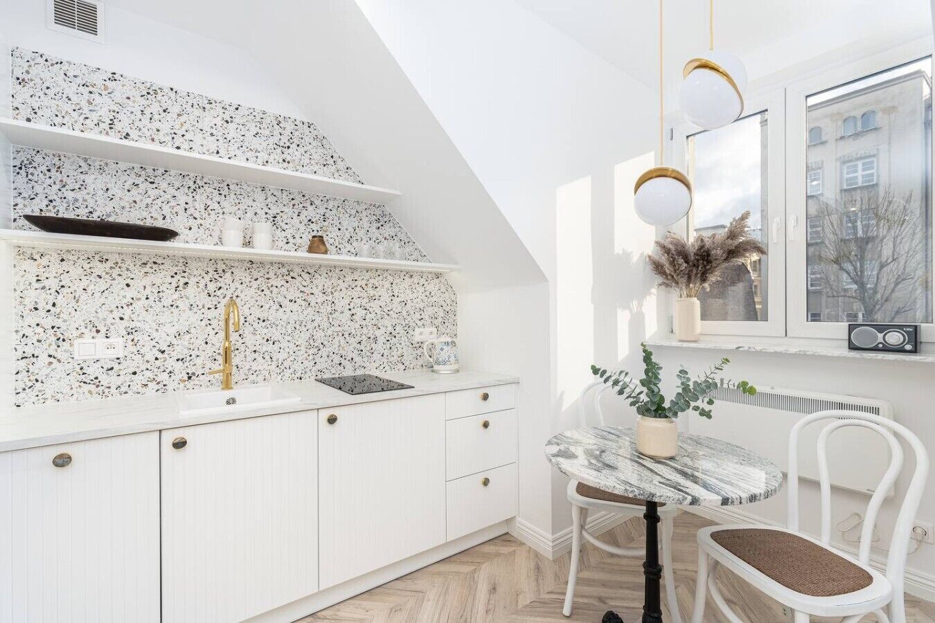 Una cocina moderna con armarios blancos, salpicadero de granito y comedor con mesa de mármol y sillas blancas.