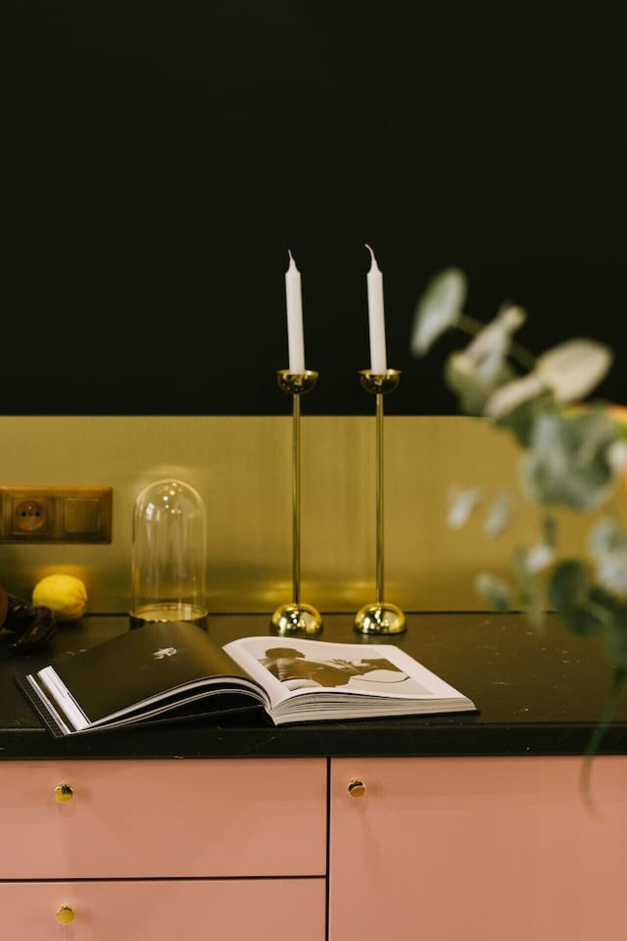 A desk with a book, two candlesticks, a glass dome, and a yellow object.