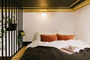 Ein Schlafzimmer mit einem Bett, Kissen, einer Decke, einer Zeitschrift und Topfpflanzen.