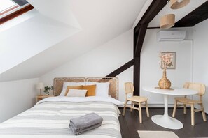 Ein Schlafzimmer mit schrägem Dach, einem Bett, einem runden Tisch mit Stühlen und einer Klimaanlage.