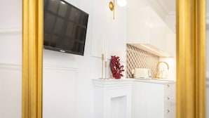 Una cocina moderna con armarios blancos, un televisor de pantalla plana sobre el mostrador y un aplique dorado.