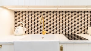 Una cocina con un lavabo blanco, un grifo dorado y un hervidor en la encimera.