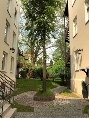 Ein Innenhof mit einem zentralen Baum, gepflasterten Wegen und angrenzenden Gebäuden mit Fenstern und Hauseingängen.
