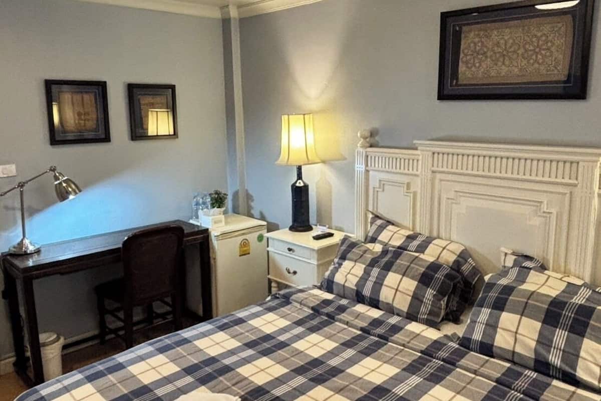 Habitación de hotel con cama, escritorio, silla, lámpara y un cuadro en la pared.