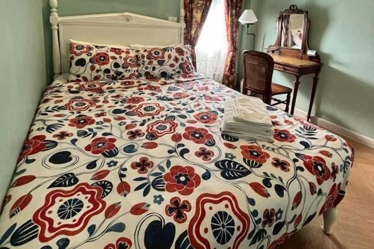 Un dormitorio con cama, mesita de noche, lámpara, silla y unidad de aire acondicionado.