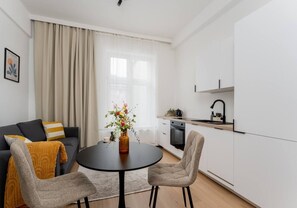 Ein modernes Wohnzimmer mit einem runden Tisch, zwei Stühlen, einem Sofa und einer Küchenzeile mit Spüle und Herd.