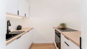 Una cocina moderna con armarios blancos, un grifo negro, una tetera, una planta y un horno empotrado.