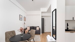 Una sala de estar moderna con un sofá, una mesa de comedor con sillas y una cocina con un lavaplatos y una encimera.