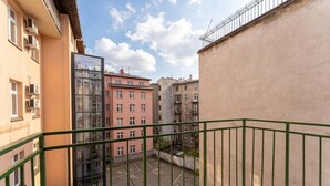 Un balcón con barandilla de metal verde que da a un patio con zona de estacionamiento y edificios colindantes.
