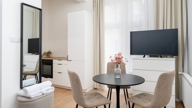 Habitación de hotel moderna con zona de comedor, televisor de pantalla plana y un amplio ventanal con cortinas.