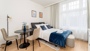 Et moderne hotelværelse med seng, rundt spisebord, to stole, et lille sofabord og en gulvlampe.