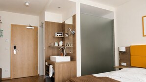 Hotellihuone, jossa on puulattia, kuviollinen päiväpeite sängyllä, kylpyhuone, jossa on pesuallas ja peili, sekä ovi, jossa on kahva.