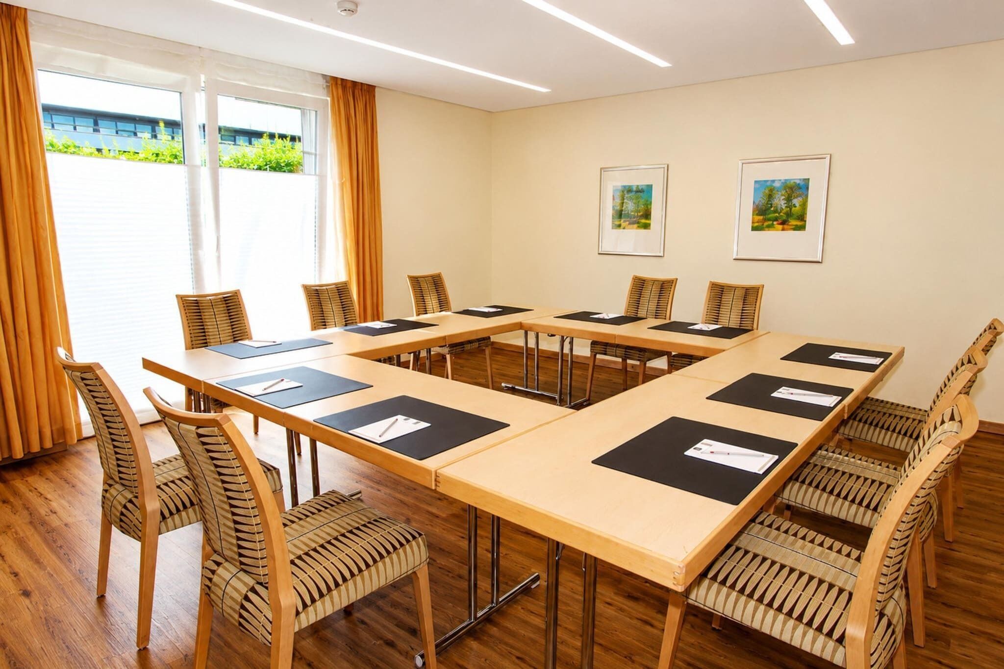 Ein Konferenzraum mit einem langen Tisch, Stühlen und zwei gerahmten Bildern an der Wand.