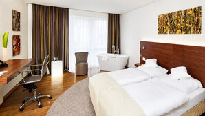 Hotellihuone, jossa on sänky, työpöytä, tuoli, pyöreä matto, kylpyamme ja ikkuna, jossa on verhot.