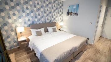 A bedroom with a bed, two bedside tables, a wall with a geometric pattern, and a door.