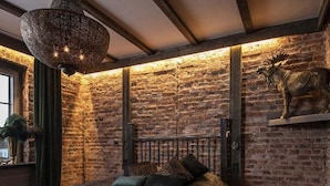 Un dormitorio con pared de ladrillo, una cama con cabecero, una lámpara colgante y una cabeza de animal montada.