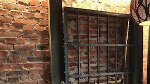 Un muro de ladrillo con una reja de metal, una cama con colcha y un control remoto sobre una mesa.
