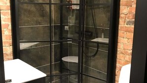 Cabina de ducha con mampara de vidrio, toallero y un estante pequeño.