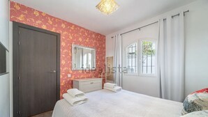 Un dormitorio con cama, cómoda, espejo, ventana con cortinas y puerta.