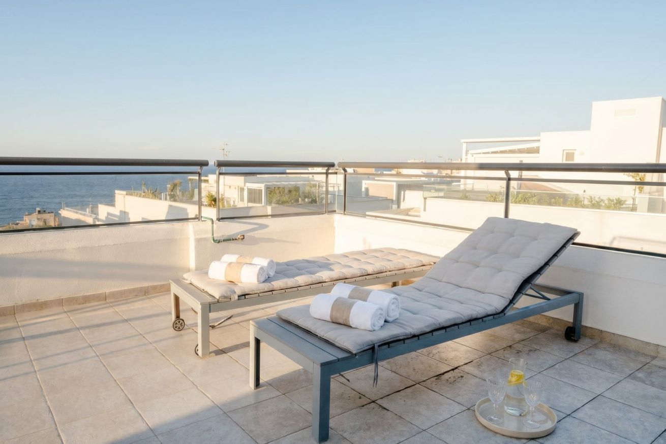 Eine Dachterrasse mit zwei Liegestühlen, einem Glastisch mit Tablett und freiem Blick auf das Meer.