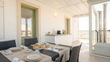 Un coin repas avec une table dressée pour quatre personnes, un comptoir de cuisine avec une machine à café, et une vue sur la mer grâce à de grandes fenêtres.