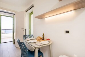 Ein Essbereich mit einem Tisch für zwei Personen, einem Stuhl mit dekorativer Rückenlehne, einer Olivenölflasche und einer Schüssel mit Cocktailtomaten.