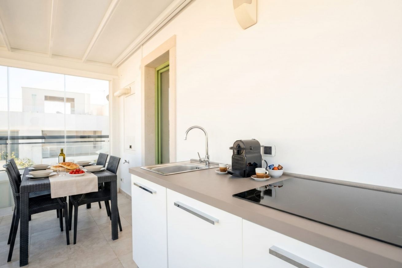 A modern kitchen with a black countertop, white cabinets, a sink, and a coffee maker.