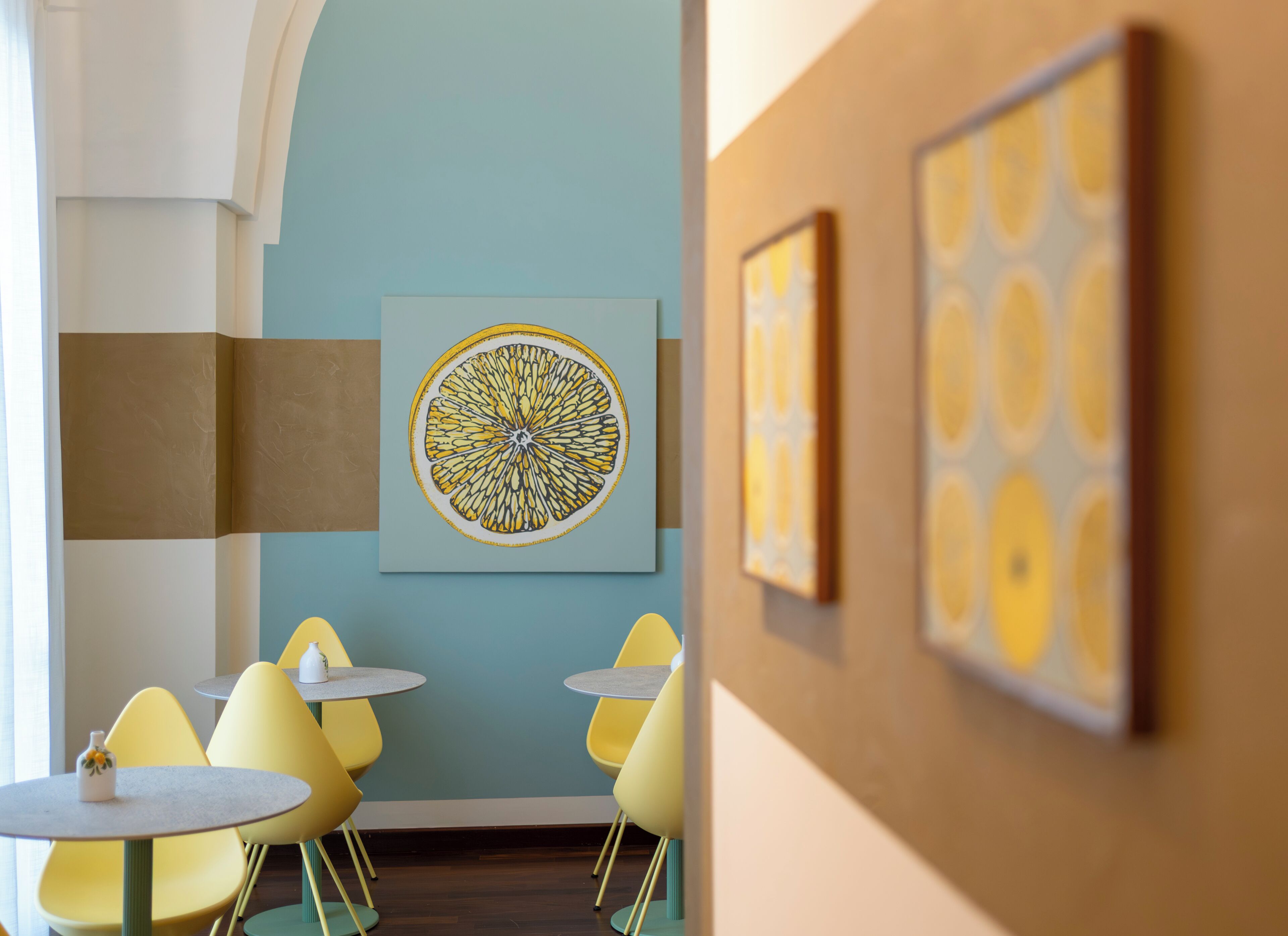 Una habitación con sillas amarillas, una mesa redonda y una gran obra de arte circular en la pared.