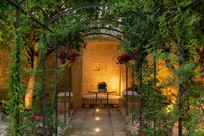 An outdoor garden area with a stone wall, a bench, and a table under a metal archway. - Rose Iconic Rooms (Lecce)