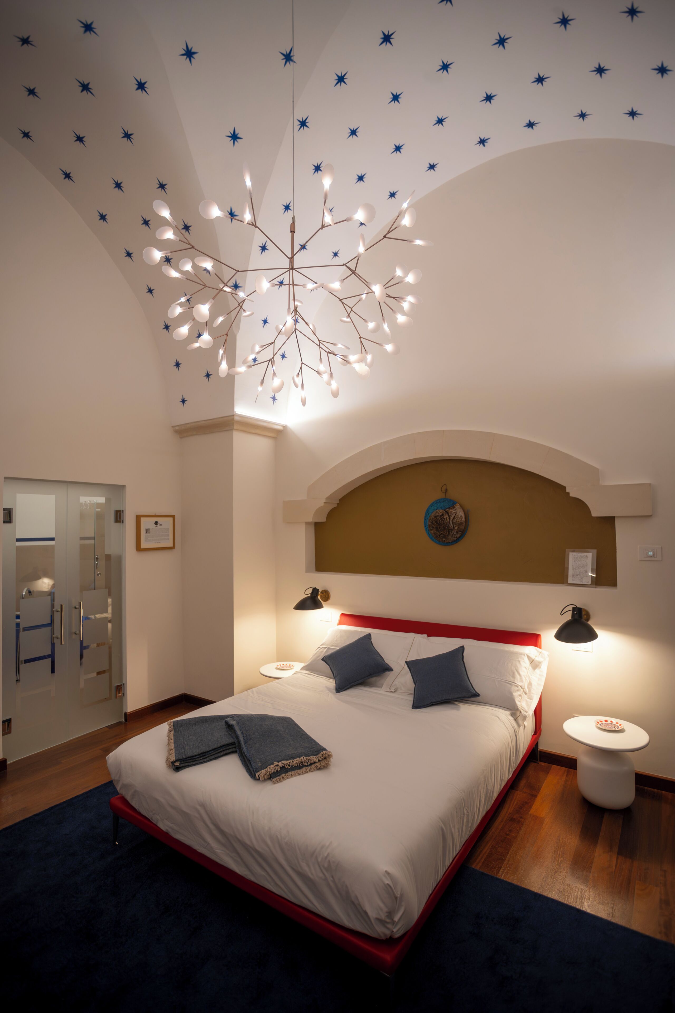 A bedroom with a bed, bedside lamps, a star-patterned ceiling, and a unique chandelier.