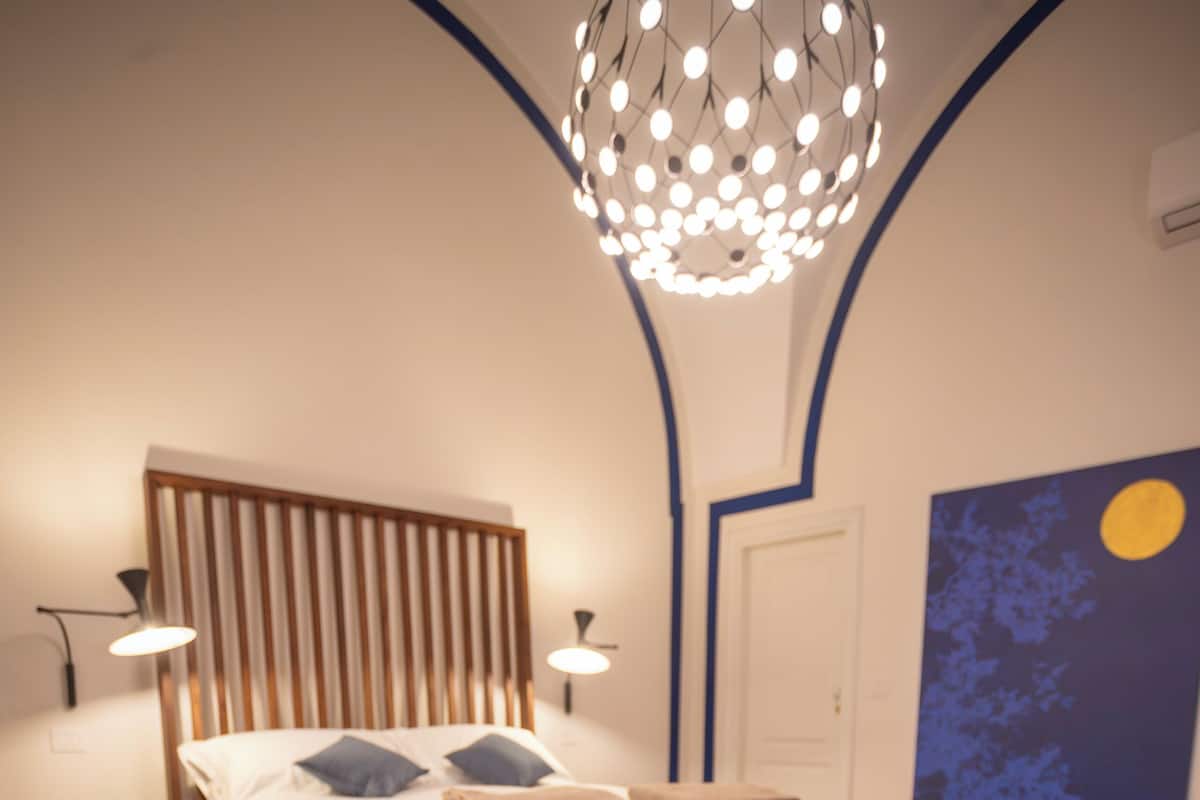 Ein Schlafzimmer mit einem Bett, Nachttischlampen, einem roten Hocker und einem Wandbild.