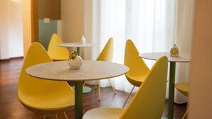 Ein Zimmer mit gelben Stühlen und Tischen, eine kleine Vase auf einem Tisch und ein Fenster mit Vorhängen.