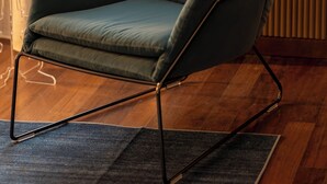 Ein moderner Sessel mit Metallgestell, platziert auf einem dunklen Teppich in einem Raum mit Holzboden und einer Heizung.