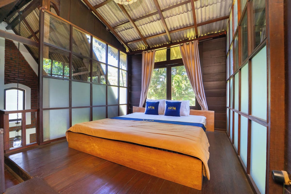 Una habitación de madera con cama, ventanas grandes y techo inclinado.