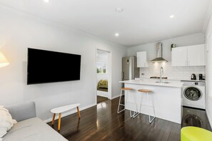 A modern kitchen with white cabinets, a built-in washing machine, and a flat-screen TV mounted on the wall.