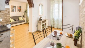 A dining area with a table set for breakfast, chairs, a sofa, and a kitchen area with a counter and cabinets. - Casa Letizia - Assisi (Tordandrea)