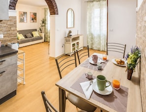 Un comedor con una mesa dispuesta para el desayuno, sillas, un sofá y una zona de cocina con encimera y armarios.