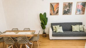 A dining area with a wooden table and chairs, a grey sofa with patterned cushions, and a large green plant. - Casa Letizia - Assisi (Tordandrea)