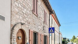 A stone building with a wooden door and shutters, a pedestrian crossing sign, and a clear sky. - Casa Letizia - Assisi (Tordandrea)