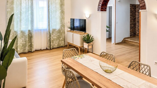 A dining area with a wooden table, woven chairs, a TV on a stand, and a potted plant. - Casa Letizia - Assisi (Tordandrea)