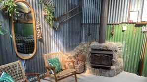Un intérieur rustique avec une cheminée en pierre, des meubles en osier et un mur en métal ondulé.