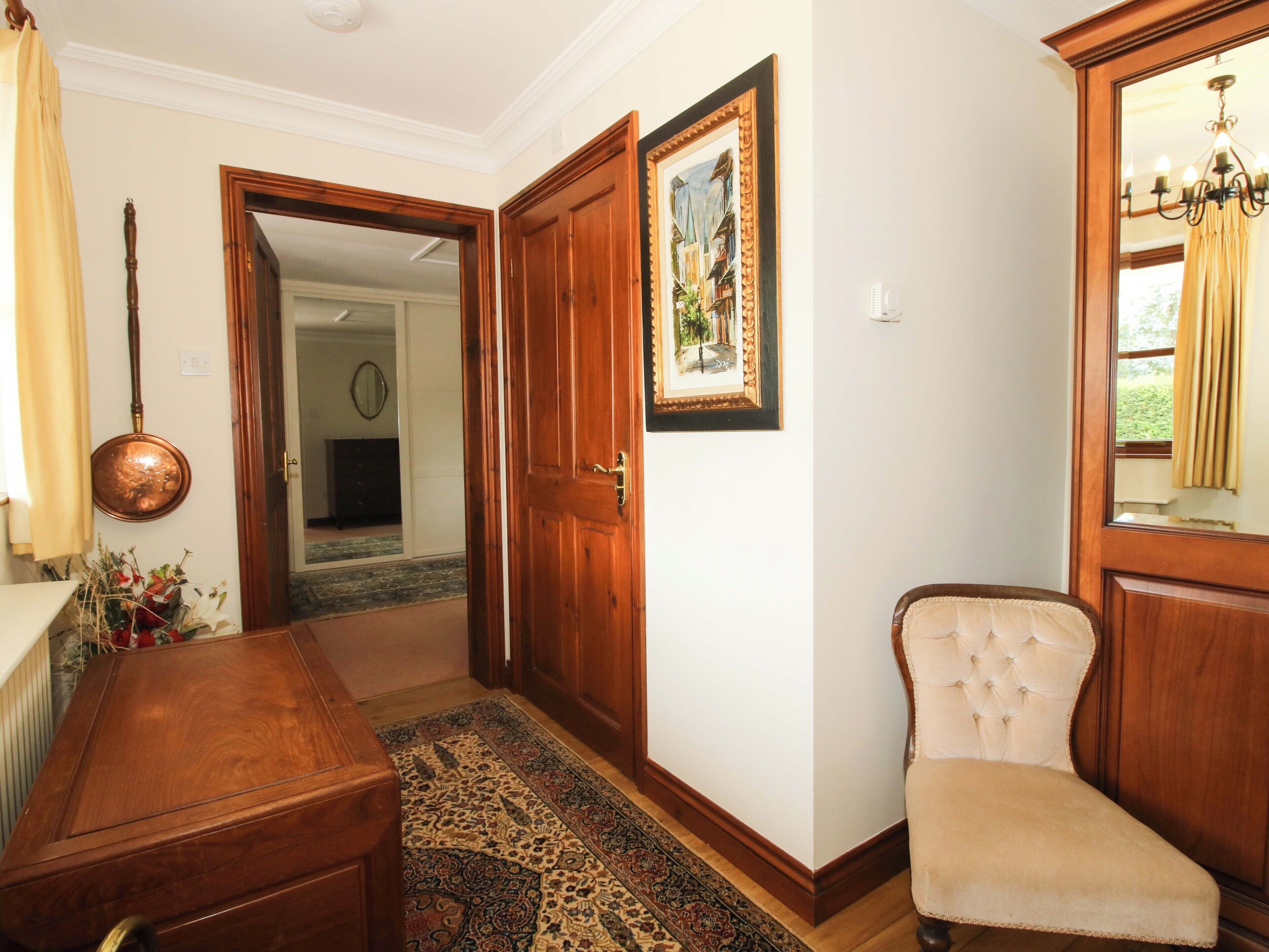 A room with a wooden desk, a chair, a patterned rug, a door, and a framed picture on the wall.