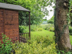 Eine Holzhütte mit Veranda, umgeben von üppiger Vegetation und einer Rasenfläche.