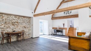 A spacious room with a stone wall, wooden beams, a dining table with chairs, a sofa, and a staircase leading to another area.