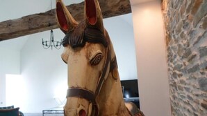 A wooden horse sculpture in a room with a stone wall, a chandelier, and a view of the outdoors.