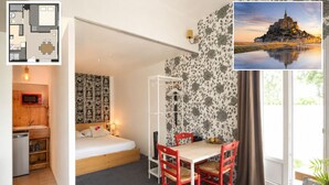 A compact room with a bed, a dining table with chairs, a small kitchenette, and a large window with a view of a castle.