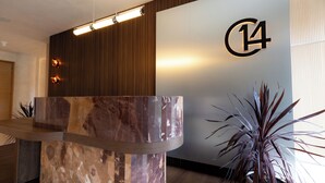 Un comptoir d’accueil avec un plateau en marbre, un mur recouvert de panneaux en bois et un grand panneau lumineux représentant le chiffre « 14 ».