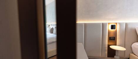 A hotel room with a bed, a bedside table, a wall-mounted light, and a small table with a lamp.