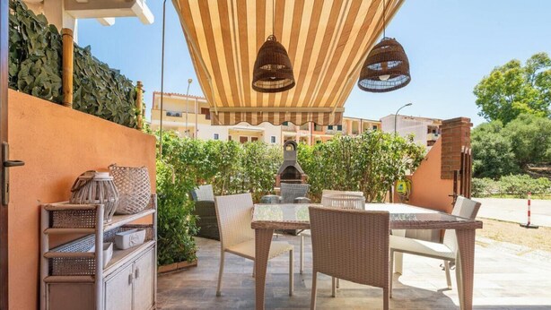 Eine Terrasse im Freien mit Korbmöbeln, einem Grill und hängenden Lichtern.