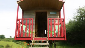 Eine kleine Holzhütte mit roter Fassade, einem Balkon mit schmiedeeisernen Geländern und einer Holztreppe zum Eingang.